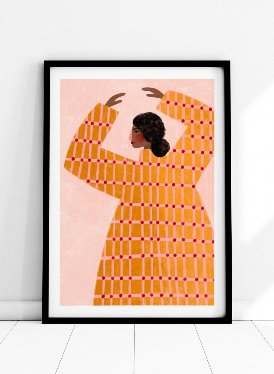 A framed art print featuring a stylized illustration of a woman in profile wearing a bright orange dress with a red grid pattern, set against a pale pink background. Dancing Woman in Orange by Bea Müller premium fine art print featuring a bold figure, warm orange tones, and a playful graphic composition.