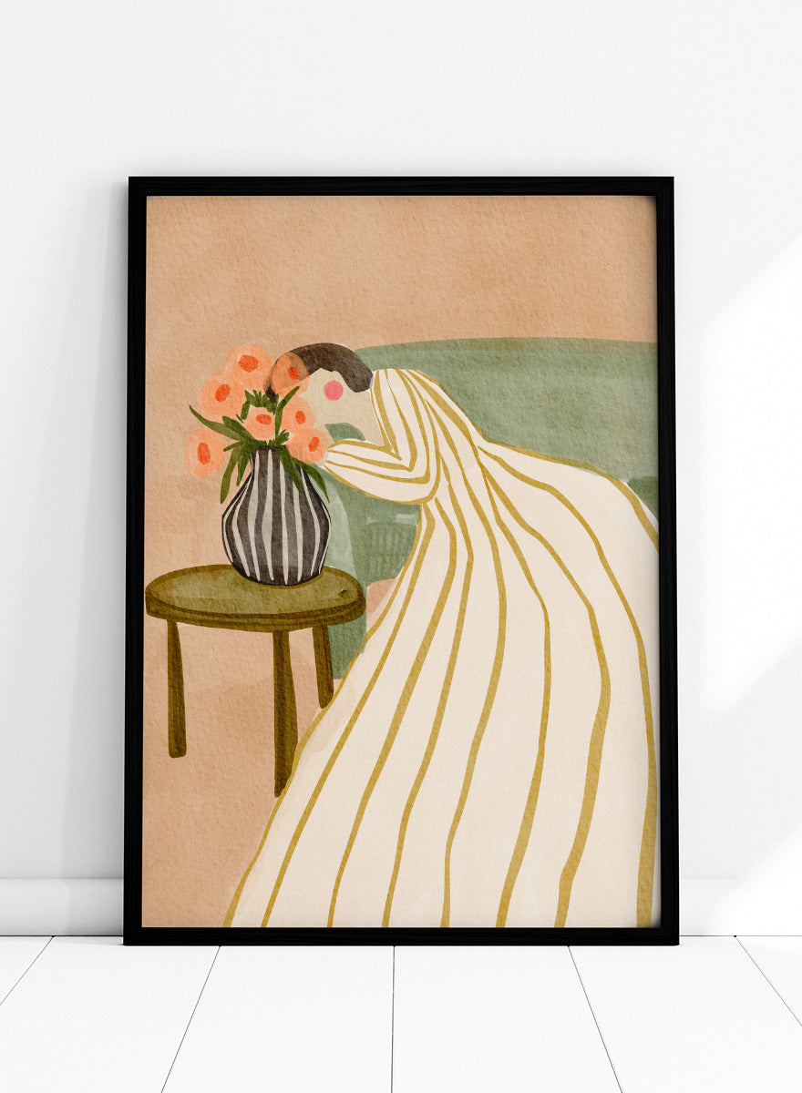 A stylized art print depicting a woman in a cream and gold striped gown leaning over a small table with a striped vase of pink flowers, set against a muted green sofa and beige background. Shop Woman Admiring Flowers by Nikita Jariwala, a modern floral wall art print featuring a woman, peach blooms, striped dress, and warm earthy tones.