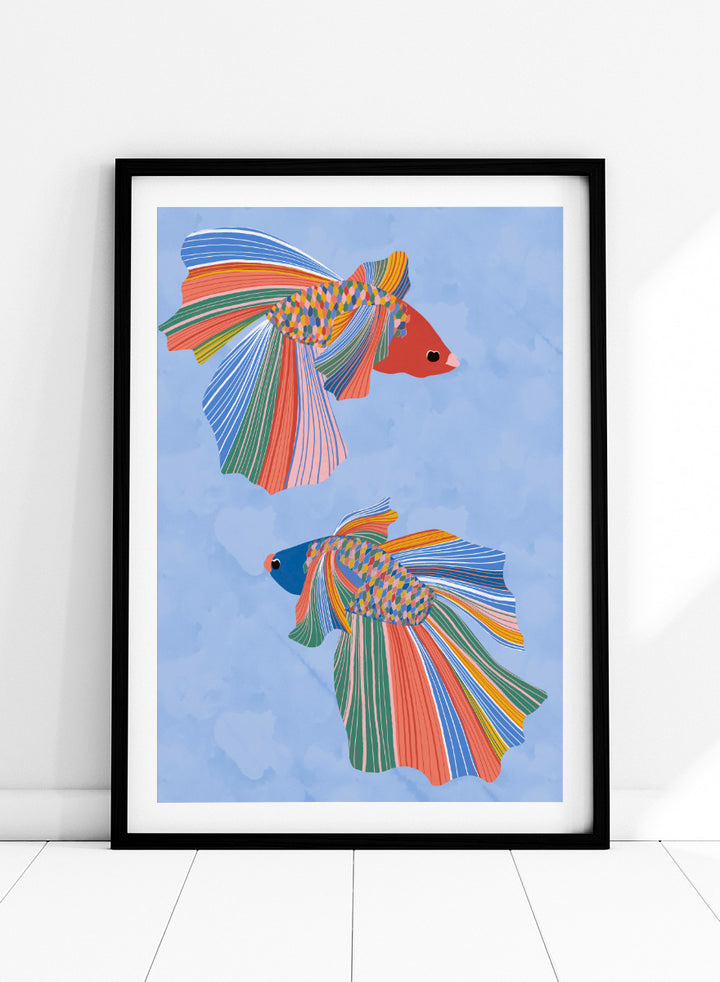 A framed art print featuring two stylized betta fish with vibrant, multicolored striped fins and bodies on a light blue water-like background. Colorful Betta Duo by Ceyda Alasar fish art print featuring two patterned betta fish with flowing fins in bright coral, blue, green, pink, and yellow.