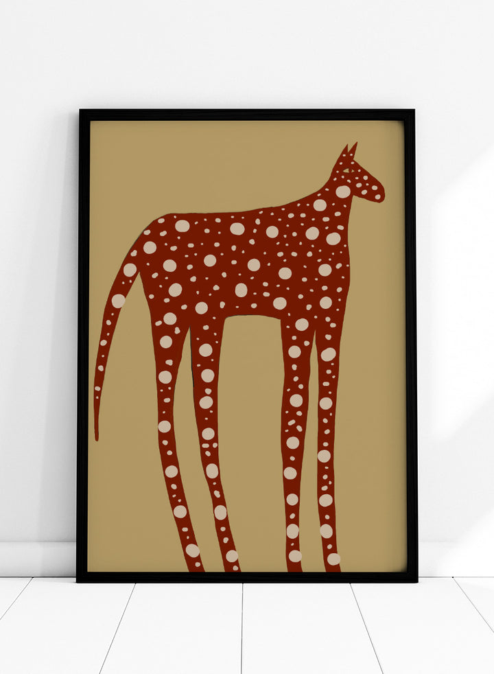 A stylized art print of a giraffe in reddish-brown with white spots, set against a tan background. Spotted Earthy Creature by The Art Concept animal art print featuring a long-legged rust-colored figure with cream spots on a muted tan background.