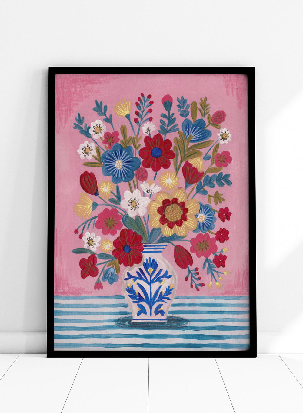 Colorful floral arrangement in a blue and white vase on a pink and blue striped background. Colorful Folk Art Bouquet by Caroline Bonne Müller is a fine art print and wall poster featuring a bright floral arrangement in a patterned vase.