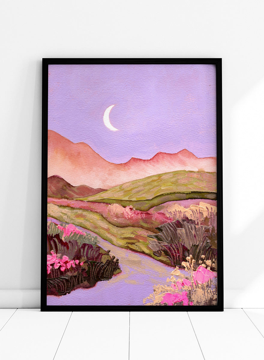 A landscape painting featuring rolling green hills, pink mountains, a purple sky with a crescent moon, and pink flowers along a winding path. Shop Moonlit Valley Path by Ekaterina Prisich, a colorful landscape art print featuring a crescent moon, winding path, rolling hills, and wildflowers.