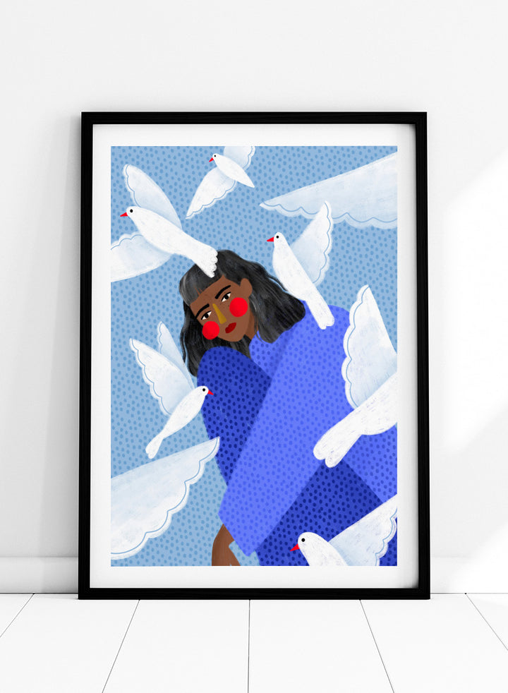 A framed art print featuring a stylized illustration of a woman with dark hair and red cheeks, wrapped in a blue patterned blanket, surrounded by white doves against a light blue dotted background. Peaceful Woman and Doves by Bea Müller art print featuring a woman in blue surrounded by white birds, layered textures, and soft modern color.