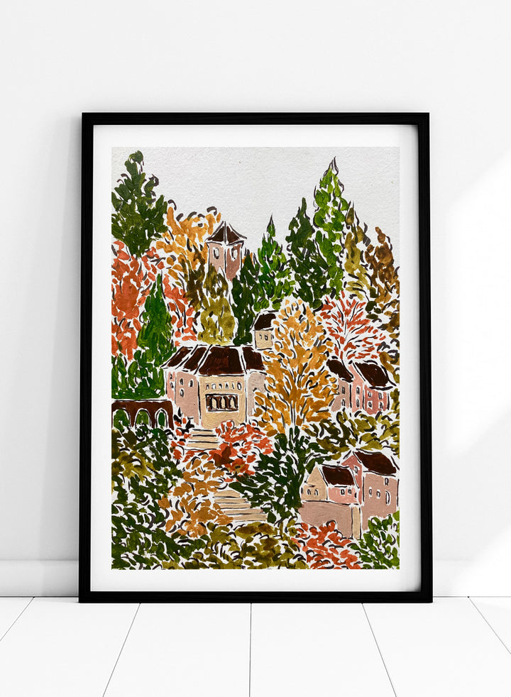 A framed art print featuring a hand-drawn, stylized landscape of a hillside village with beige buildings, brown roofs, and dense trees in green, yellow, orange, and red tones. Shop Autumn Hillside Village by Rushati Chowdhury, a colorful autumn landscape art print with hillside homes, winding steps, dense trees, and warm fall tones.