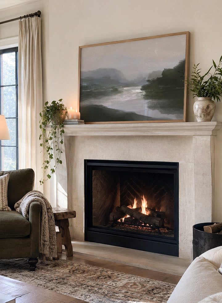 A framed landscape art print depicting a misty river scene with dark green hills, a reflective river, and a pale gray sky. Shop Tranquillitas by Dan Hobday, a contemporary landscape wall art print featuring reflective water, distant hills, dark green trees, and soft gray tones.