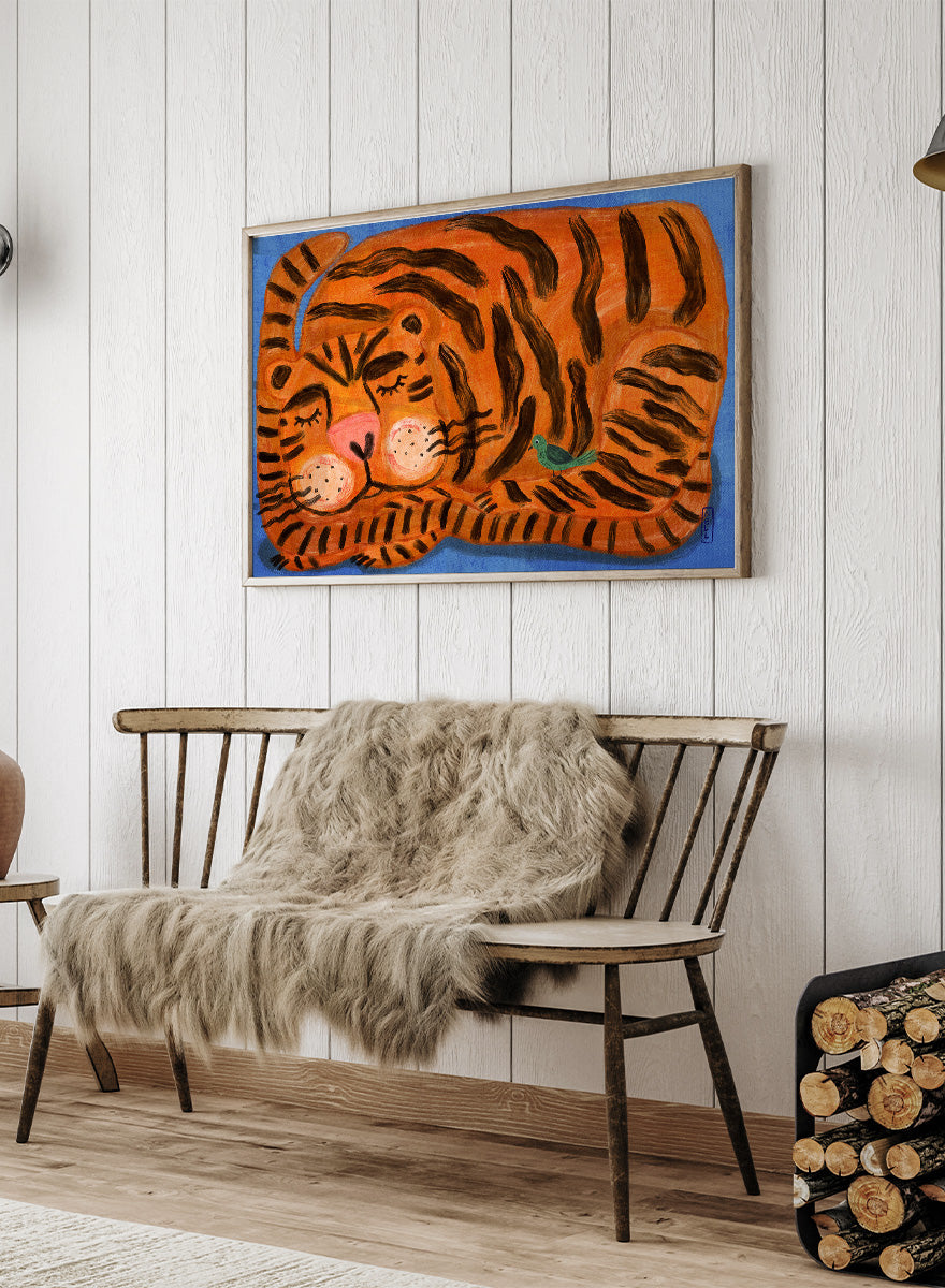 A framed painting of a sleeping tiger on a blue background. The tiger is orange with bold black stripes, has a pink nose and cheeks, and a small green bird near its side. A framed painting of a sleeping tiger on a blue background. The tiger is orange with bold black stripes, has a pink nose and cheeks, and a small green bird near its side. 
