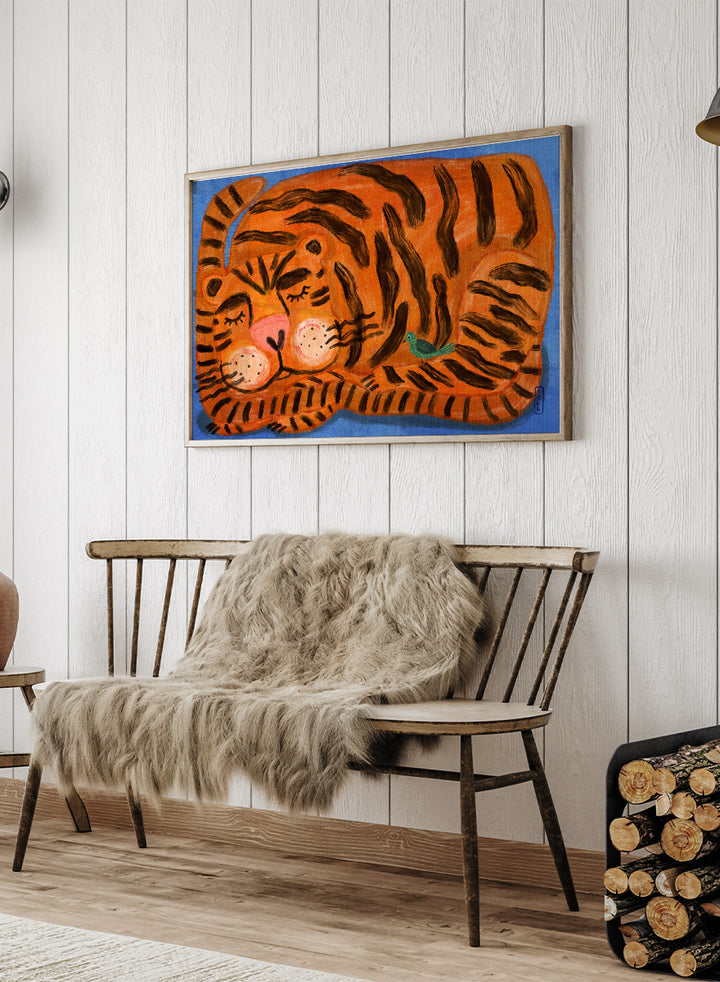 A framed painting of a sleeping tiger on a blue background. The tiger is orange with bold black stripes, has a pink nose and cheeks, and a small green bird near its side. A framed painting of a sleeping tiger on a blue background. The tiger is orange with bold black stripes, has a pink nose and cheeks, and a small green bird near its side. 