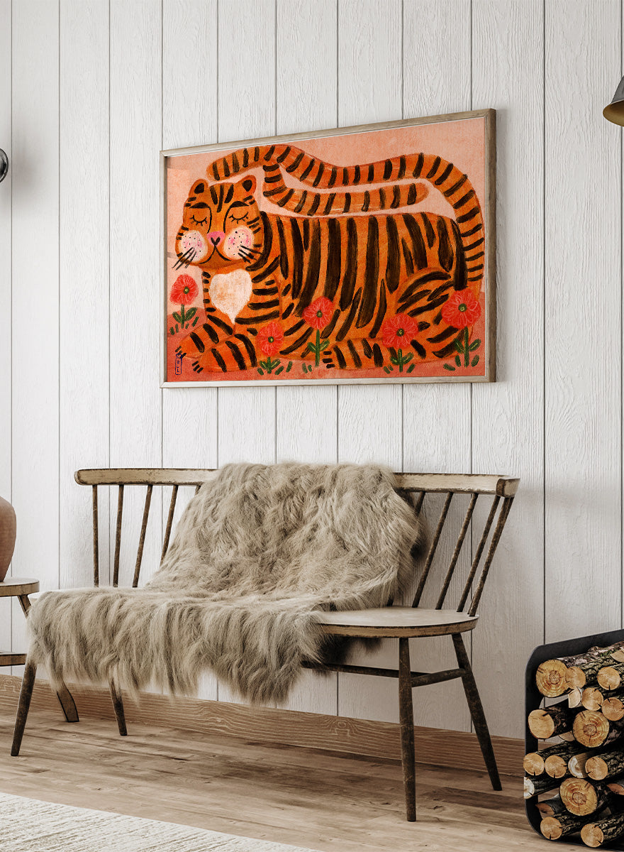 A framed art print featuring a stylized orange and black striped tiger lying among red flowers on a peach background. Playful tiger animal art print by Dirkie Nell with bold orange stripes, red poppies, and a warm peach background. Shop this cheerful piece today.