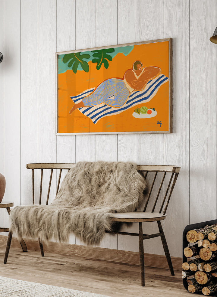Framed artwork of a woman lounging on a towel with a plate of fruit against an orange background. A Day at the Beach by Arty Guava is a colorful coastal art print featuring a relaxed beach scene, tropical foliage, bold color, and contemporary illustration.