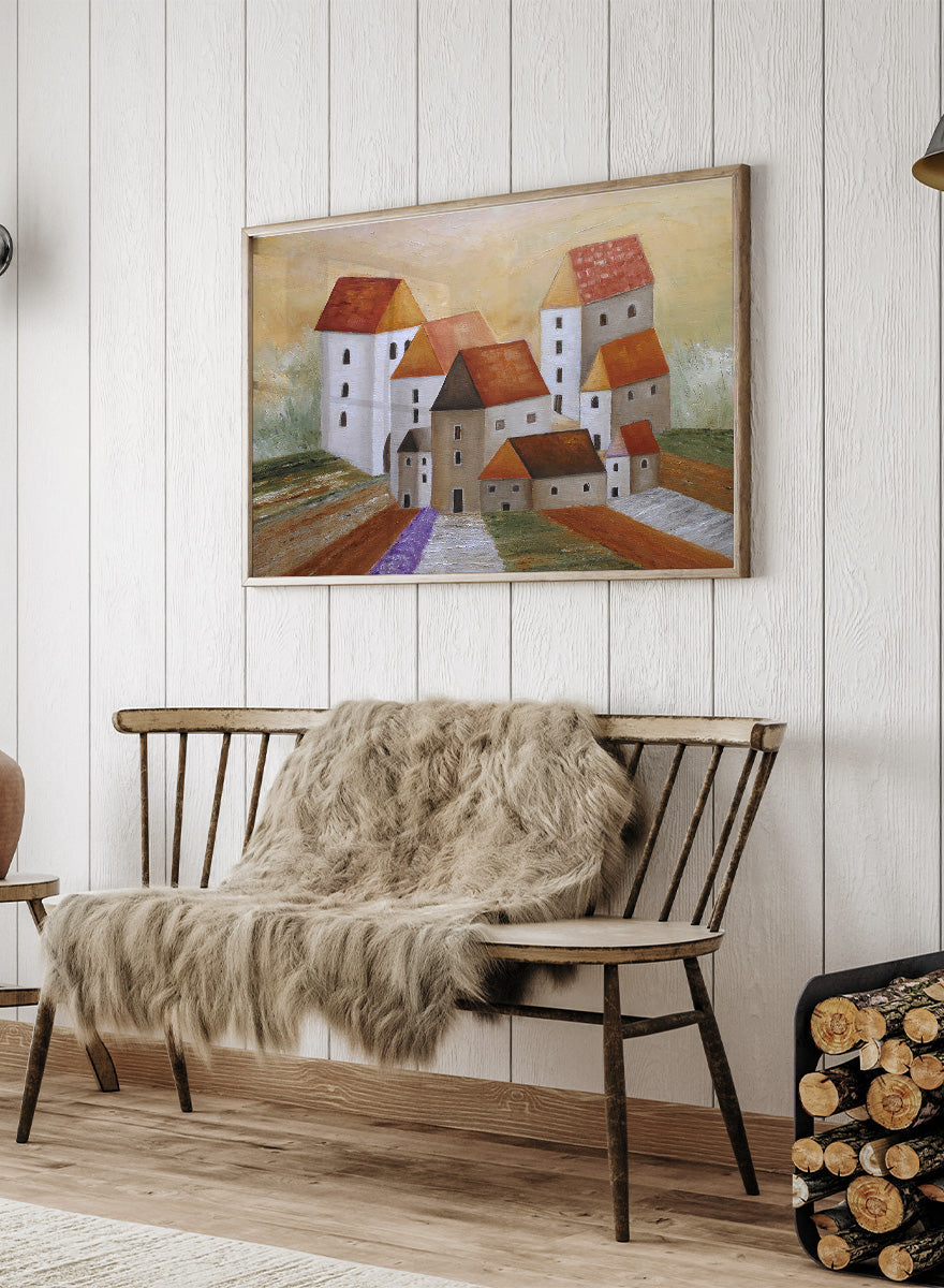 A framed landscape painting depicting stylized white buildings with orange-brown roofs, set in a field with a purple path under a warm yellow sky. Shop Peaceful Lavender Village by Angeles M. Pomata, an autumn village landscape art print featuring white houses, terracotta roofs, lavender fields, and warm earthy tones.