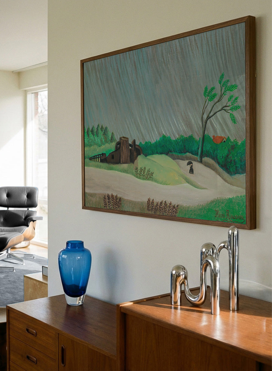 A framed landscape painting depicting a rainy day in a green valley with a small house, a lone tree, and a figure holding an umbrella. A Rainy Morning by Henri Rousseau is a vintage landscape art print featuring a rainy country road, umbrella figure, green fields, trees, and a rustic watermill.