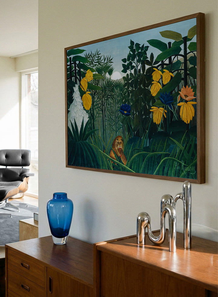 A framed art print depicting a lush jungle scene with green foliage, yellow flowers, blue and orange blossoms, and a small lion near the bottom center. The Repast of the Lion by Henri Rousseau is a vintage jungle art print featuring a lion hidden among dense tropical foliage and lush green plants.