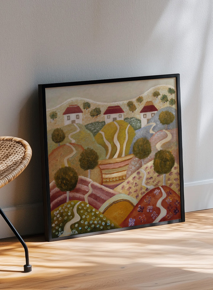 A framed landscape painting featuring stylized rolling hills, winding paths, small houses with red roofs, and trees. Shop Charming Hillside Village by Angeles M. Pomata, a colorful countryside art print featuring winding paths, red-roof houses, flowering fields, and warm autumn tones.