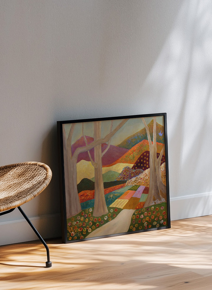 A framed landscape painting featuring stylized trees, a winding path, patchwork fields, and mountains in warm earthy tones. Shop Colorful Field Path by Angeles M. Pomata, an autumn landscape art print featuring a winding path, textured fields, flowers, and rolling countryside.