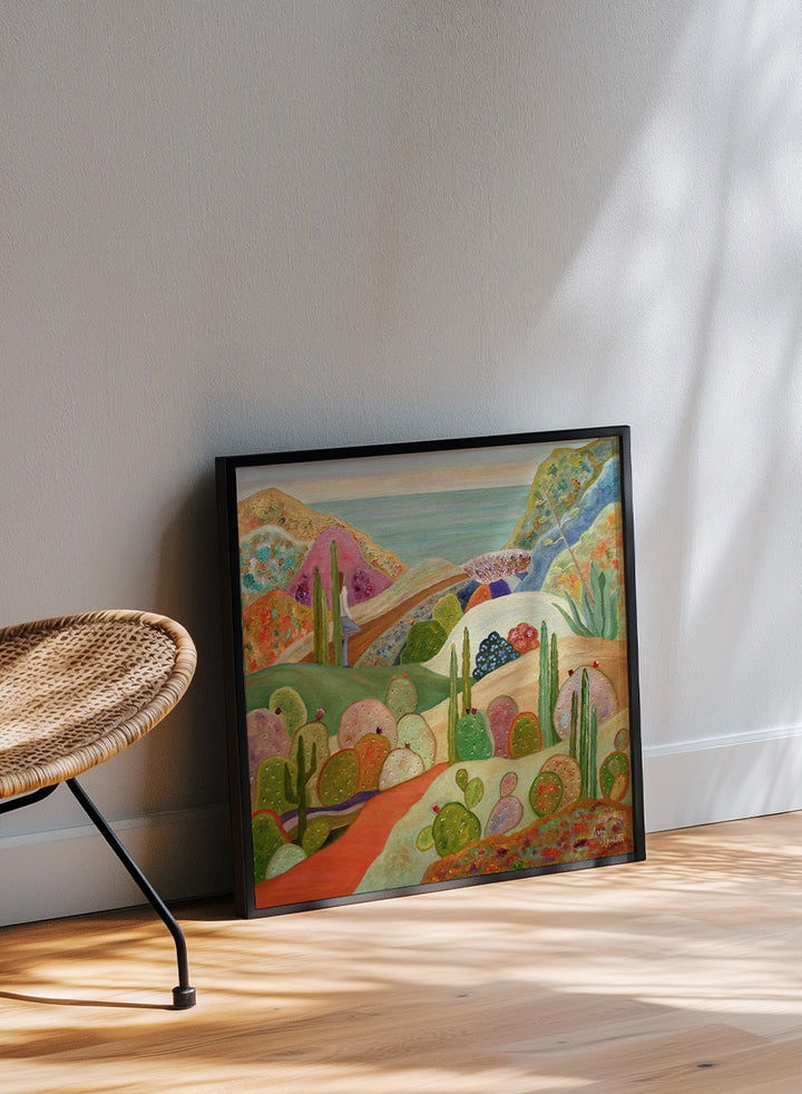 A framed colorful landscape painting featuring stylized cacti, hills, and a coastal scene. Shop Colorful Desert Yoga View by Angeles M. Pomata, a colorful desert landscape art print featuring cacti, rolling hills, a yoga figure, and coastal views.