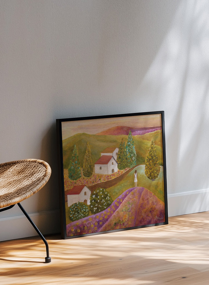 A framed landscape painting featuring rolling green hills, white houses with red roofs, tall conical trees, and a figure standing on a purple field. Shop Woman in Lavender Fields by Angeles M. Pomata, a colorful landscape and figurative art print featuring lavender fields, white houses, cypress trees, and rolling hills.