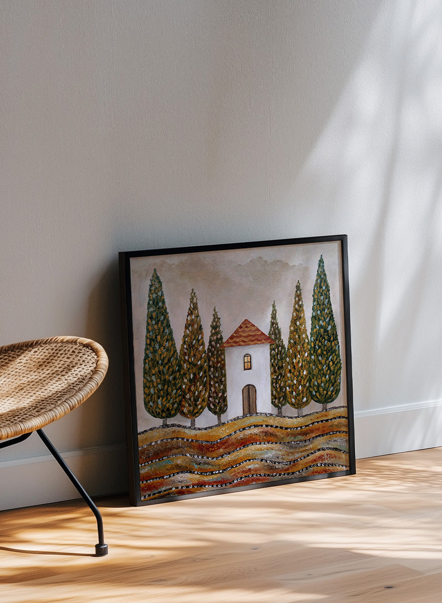 A framed landscape art print depicting a small white house with a red-tiled roof, surrounded by tall green cypress trees and wavy golden-brown hills. Shop Tuscan Cypress House by Angeles M. Pomata, an autumn landscape art print featuring a white country house, tall cypress trees, terracotta roof, and warm earthy tones.
