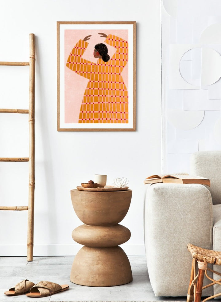 A framed art print featuring a stylized illustration of a woman in profile wearing a bright orange dress with a red grid pattern, set against a pale pink background. Dancing Woman in Orange by Bea Müller premium fine art print featuring a bold figure, warm orange tones, and a playful graphic composition.