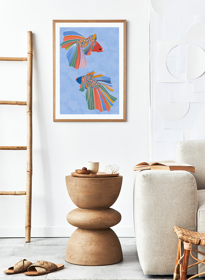 A framed art print featuring two stylized betta fish with vibrant, multicolored striped fins and bodies on a light blue water-like background. Colorful Betta Duo by Ceyda Alasar fish art print featuring two patterned betta fish with flowing fins in bright coral, blue, green, pink, and yellow.