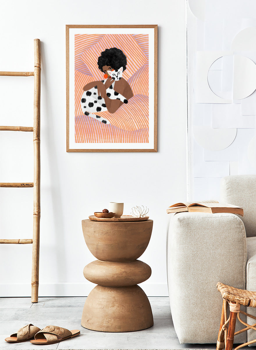 A framed art print featuring a stylized illustration of a person with an afro holding a black-and-white spotted cat, set against a peach and orange striped background. Cozy Cat Cuddles by Bea Müller animal art print featuring a woman embracing a spotted cat among soft peach and lilac stripes for cozy pet lover decor.