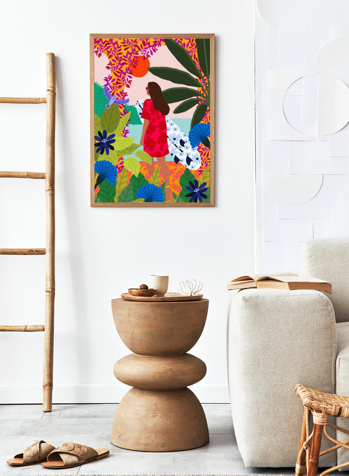 Woman in a red dress with a white surfboard amidst tropical foliage and flowers. Going Surfing by Rafaela Mascaro is a colorful tropical art print featuring a surfer, lush botanicals, vibrant florals, and sunny coastal inspiration.
