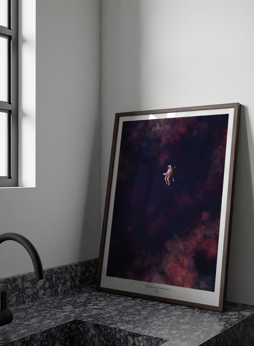 A framed art print featuring an astronaut floating in a starry outer space scene with deep purple, pink, and blue nebulae. The print has a white border with the text &