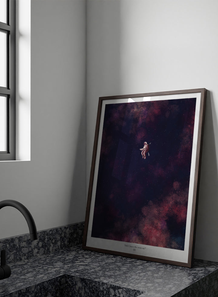 A framed art print featuring an astronaut floating in a starry outer space scene with deep purple, pink, and blue nebulae. The print has a white border with the text &