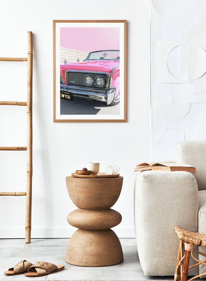 Pink vintage car with 'I ❤️ YOU' license plate against a pink sky. P.S. I Love You by Tom Windeknecht is officially licensed photography featuring a vibrant pop-art style photo of a car with romantic typography. Framed or unframed.