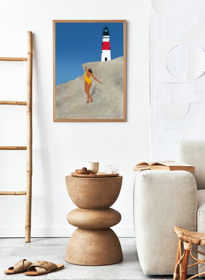 Woman in a yellow swimsuit standing on a rocky outcrop with a lighthouse in the background. My Beach by Jota de Jai is a modern coastal wall art print featuring a woman in a yellow swimsuit and a lighthouse. Officially licensed fine art poster with optional wood frame.
