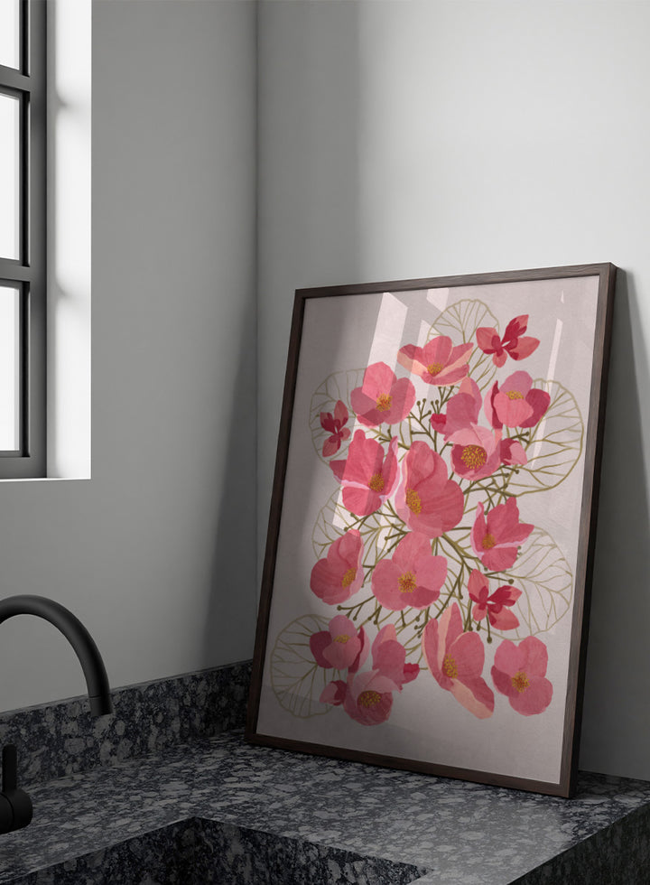 A framed botanical art print featuring pink flowers with yellow centers and delicate gold leaf outlines on a pale pink background. Shop Japanese Quince Floral Art Print by Katie O&