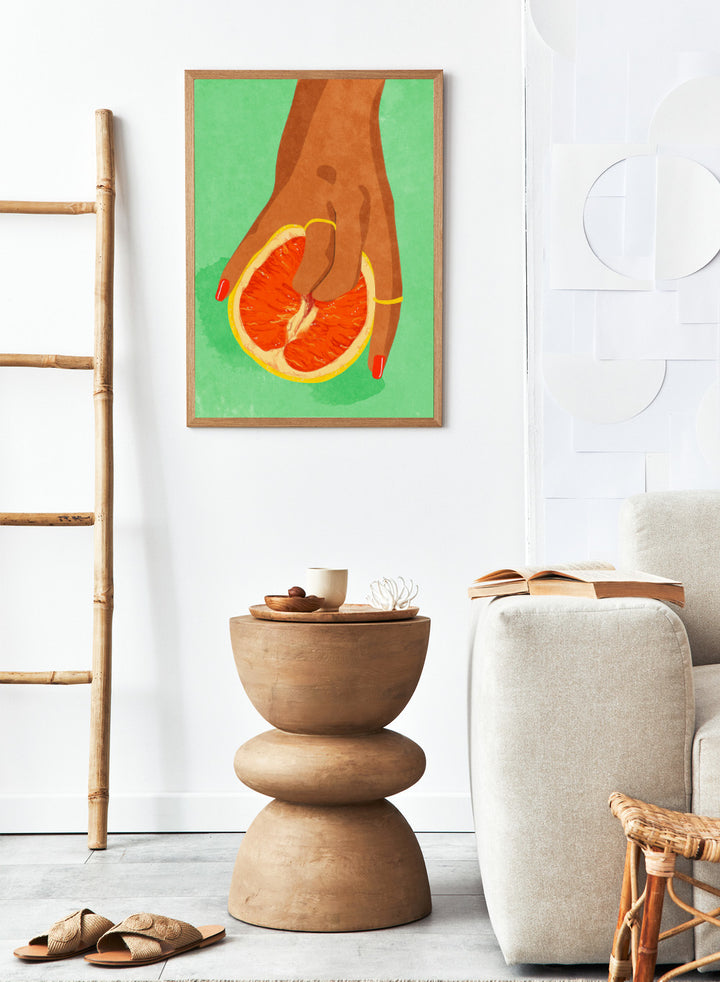 Illustration of a hand holding a sliced orange against a green background. Fruit Lover wall art print by Raissa Oltmanns blends playful citrus and intimate symbolism in a contemporary modern aesthetic poster.
