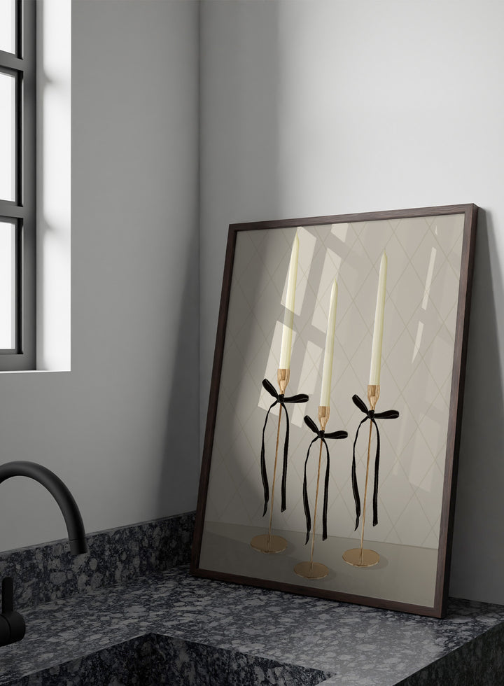 Three gold taper candle holders with cream candles and black ribbon bows, arranged on a light gray surface against a beige diamond-patterned background. Elegant Gold Taper Candles by Lisa Solomoniuk premium framed fine art print featuring gold candlesticks, cream tapers, and long black ribbons.