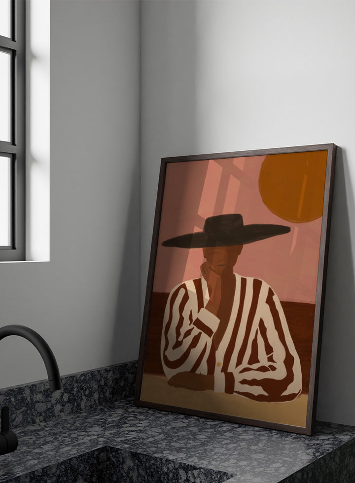 A stylized art print depicting a seated figure in a wide-brimmed black hat and a brown-and-white vertically striped shirt, set against a dusty pink sky with a large orange sun. Desert Dreamer by The Art Concept art print featuring a relaxed figure in a wide black hat, striped shirt, dusty pink sky, and warm desert-inspired tones.