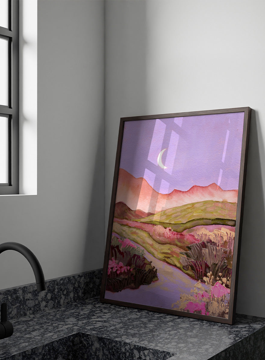 A landscape painting featuring rolling green hills, pink mountains, a purple sky with a crescent moon, and pink flowers along a winding path. Shop Moonlit Valley Path by Ekaterina Prisich, a colorful landscape art print featuring a crescent moon, winding path, rolling hills, and wildflowers.