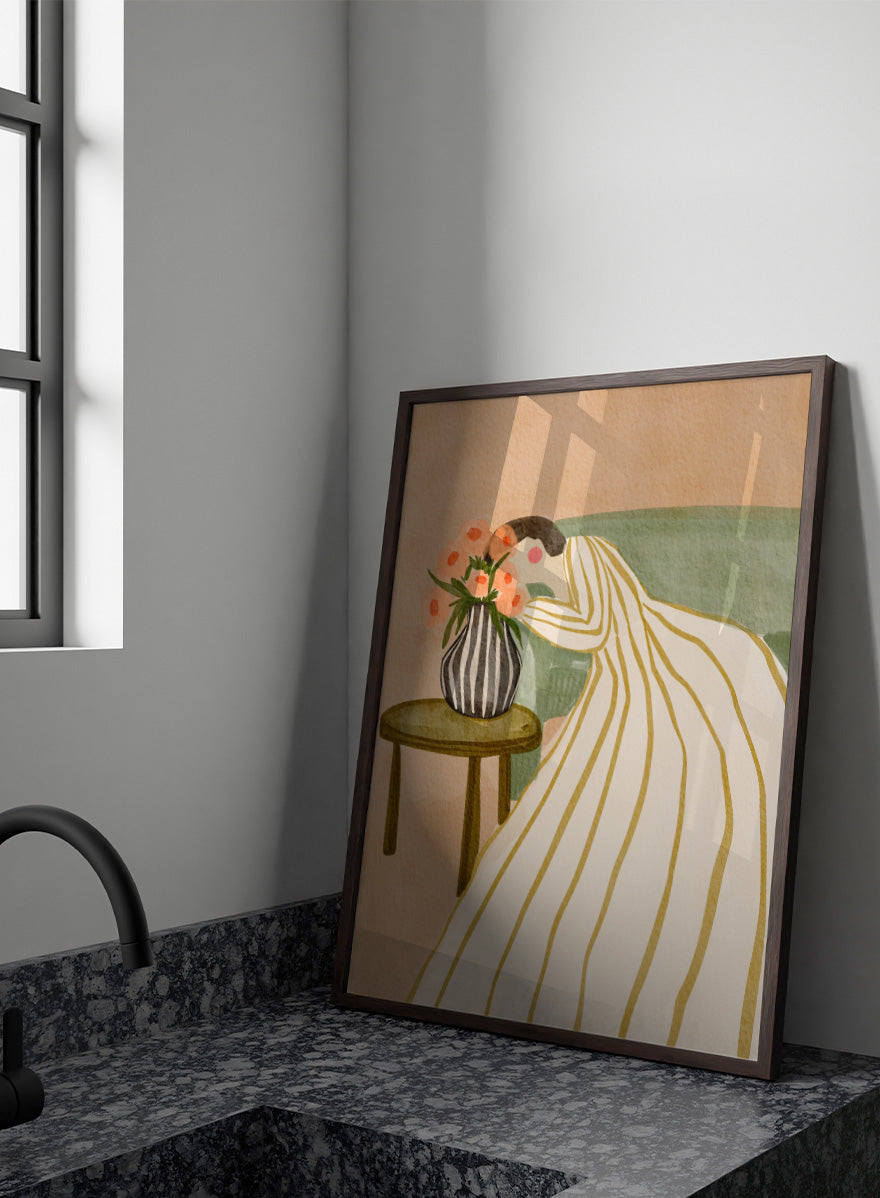 A stylized art print depicting a woman in a cream and gold striped gown leaning over a small table with a striped vase of pink flowers, set against a muted green sofa and beige background. Shop Woman Admiring Flowers by Nikita Jariwala, a modern floral wall art print featuring a woman, peach blooms, striped dress, and warm earthy tones.