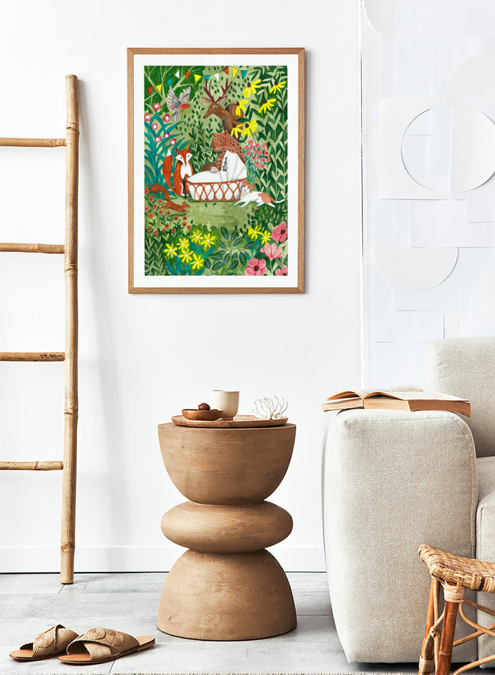 A framed art print featuring a whimsical forest illustration with animals gathered around a basket, surrounded by flowers and foliage. The print is shown with a white mat and a black frame against a white background. Welcome to the Forest by Caroline Bonne Müller woodland animal art print featuring a baby surrounded by a leopard, fox, deer, cat, flowers, and forest life.