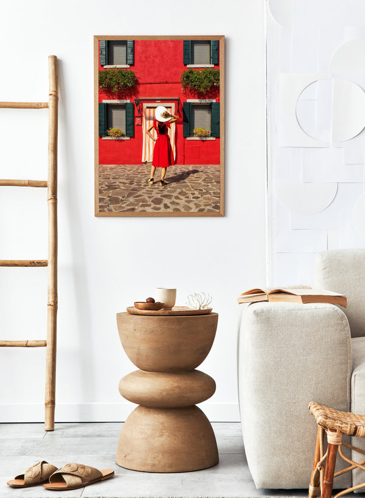 Woman in a red dress and white hat standing in front of a red wall with green shutters. Red Art Print by Anette Ohlendorf featuring a woman in a red dress standing against a red building. Officially licensed travel photography with strong color and symmetry.
