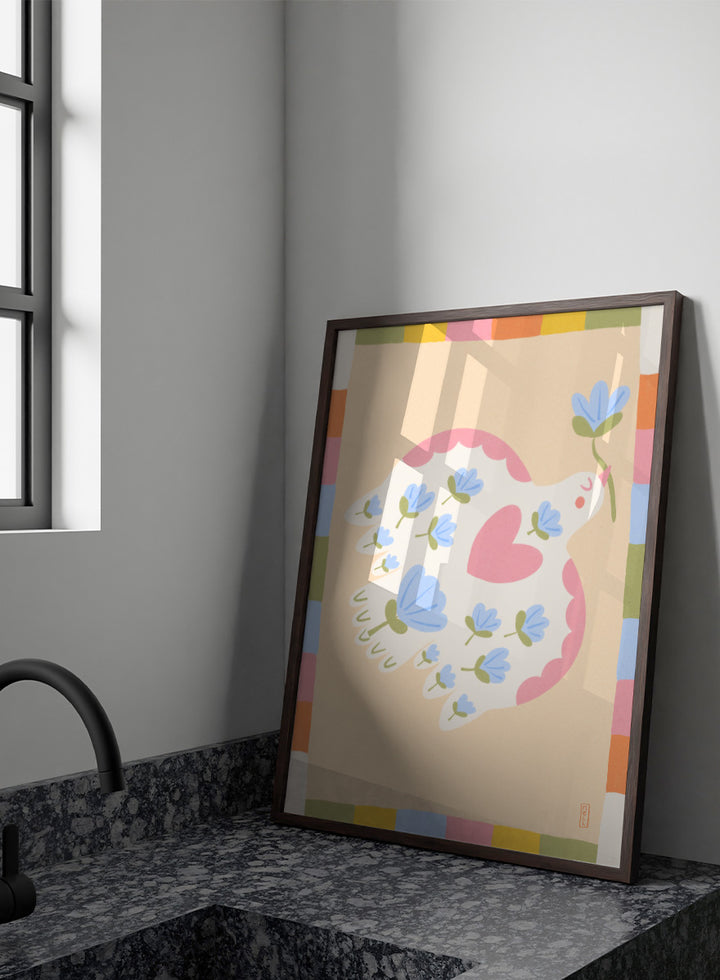 A framed art print featuring a whimsical illustration of a white dove with blue flowers and a pink heart, framed by a pastel multicolor border on a light peach background. Shop Flowering Peace Dove by Dirkie Nell, a colorful bird and floral art print featuring a white dove, blue flowers, pink wings, and a playful peace motif.