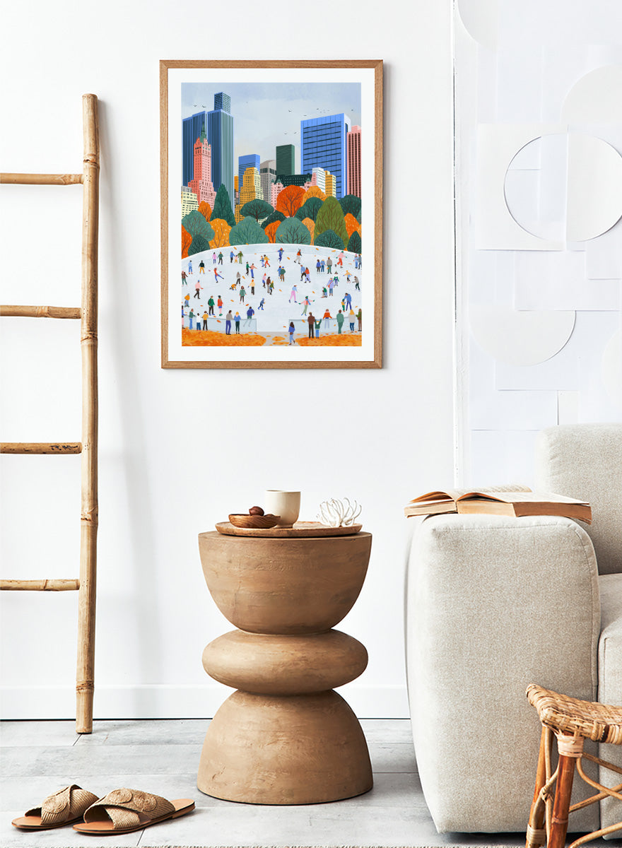 A framed art print depicting a city skyline with autumn trees and a large white ice rink filled with small illustrated people skating. Autumn City Ice Skating by Ceyda Alasar city art print featuring a lively outdoor rink, fall trees, skaters, and a colorful urban skyline.