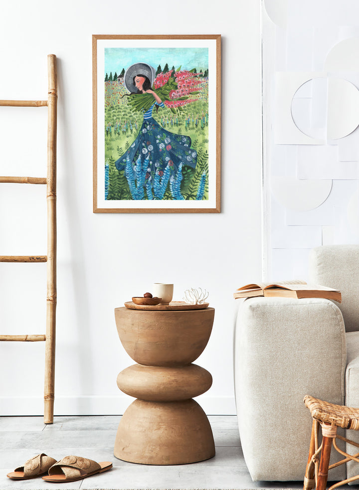 Woman in a floral dress holding flowers in a garden. Woman With Summer Flowers by Caroline Bonne Müller is a fine art print and wall poster featuring a woman carrying flowers through a colorful field.