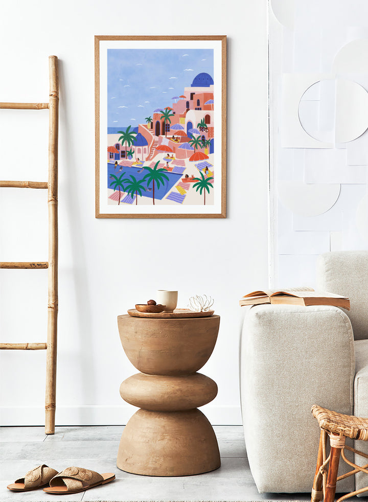 A stylized art print depicting a Mediterranean resort scene with palm trees, beach umbrellas, lounge chairs, a swimming pool, and pastel-colored buildings under a light blue sky. Mediterranean Poolside Retreat by Ceyda Alasar travel art print featuring a colorful coastal resort, palm trees, sunbathers, striped umbrellas, and sea views.