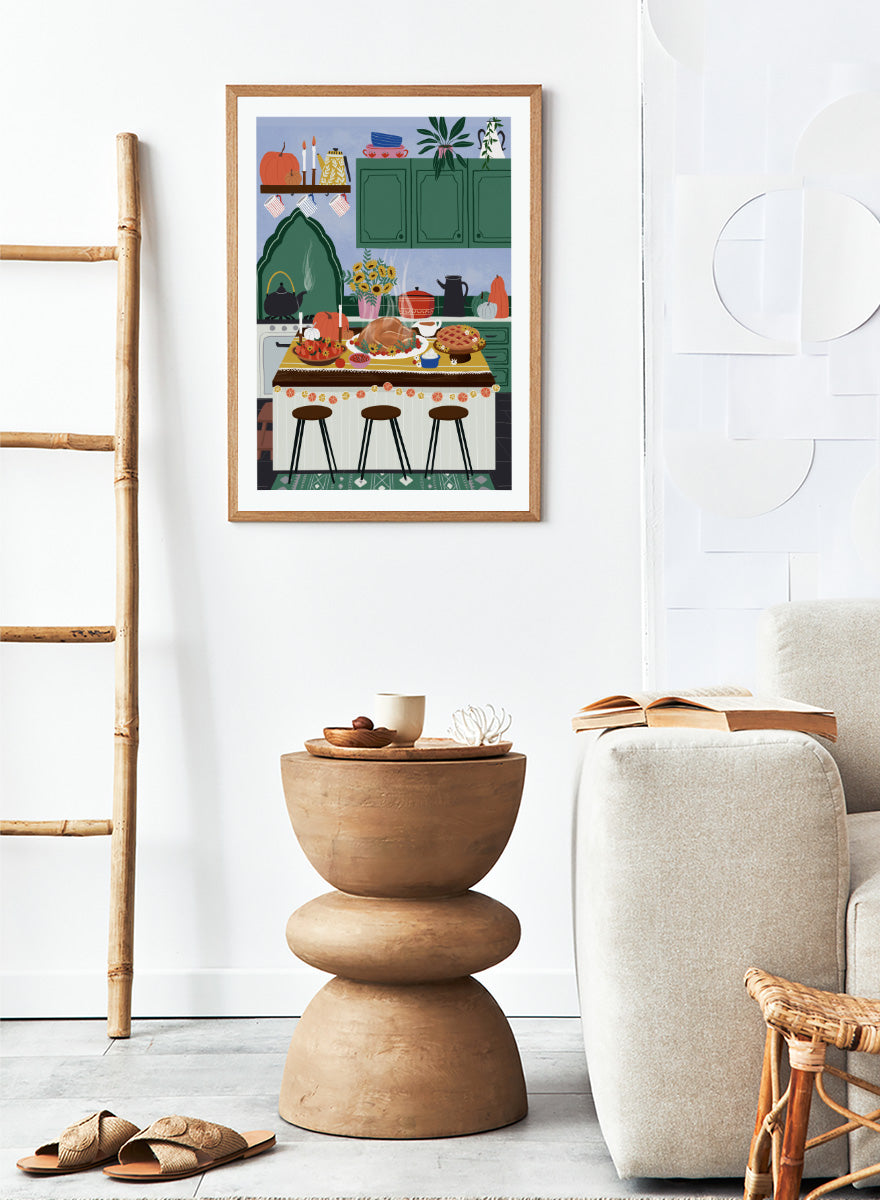 A framed art print depicting a cozy, stylized autumn kitchen scene with a large roasted turkey on a table covered in fall dishes, green cabinets, pumpkins, and three bar stools. Cozy Thanksgiving Kitchen by Ceyda Alasar kitchen art print featuring a turkey feast, pie, pumpkins, flowers, candles, and warm autumn decor.