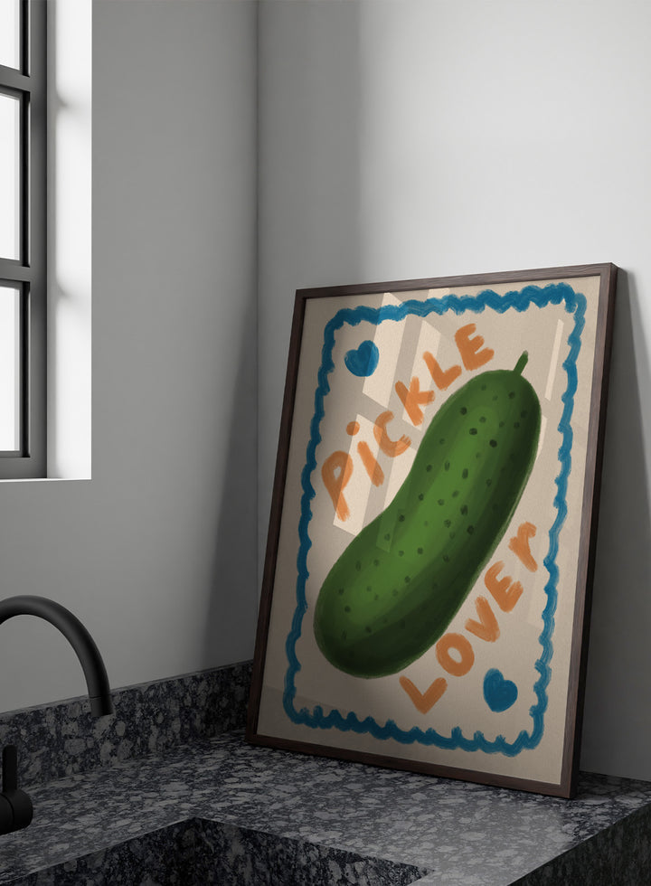 An art print featuring a hand-drawn green pickle centered on a cream background, surrounded by a blue scalloped border. The words &