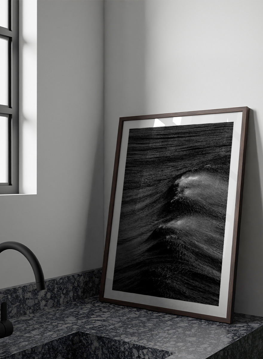 Black and white fine art photographic print of ocean waves, featuring a dramatic wave crest with white foam against dark textured water. Night Wave Cascade by Shot by Clint black-and-white ocean photography print featuring dark rolling waves, sea spray, and dramatic natural movement.