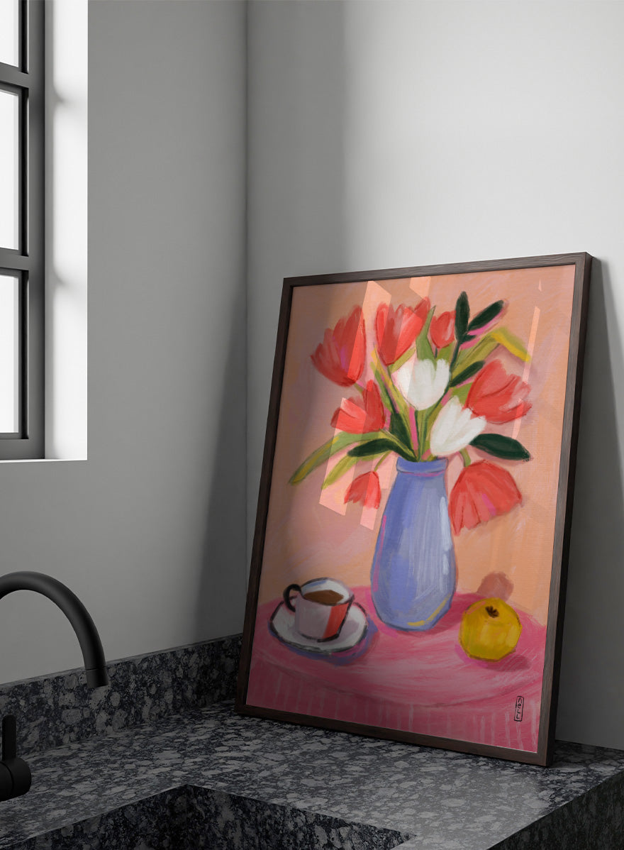 A still life painting of a bouquet of red and white tulips in a blue vase, set on a pink tablecloth next to a cup of coffee and a yellow fruit, against a peach background. Shop Fresh Tulips and Coffee by Dirkie Nell, a colorful floral still life art print featuring tulips, coffee, a blue vase, and warm pink and peach tones.