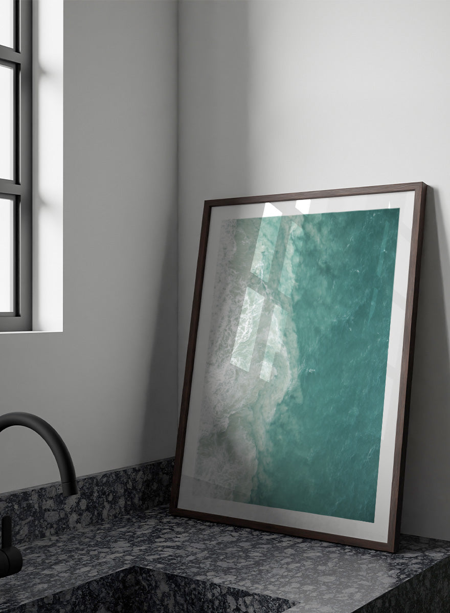 A framed aerial photograph of ocean waves, showing white foam breaking into turquoise and teal water. Ocean’s Edge by Shot by Clint aerial ocean photography print featuring turquoise water, white surf, and layered coastal movement.