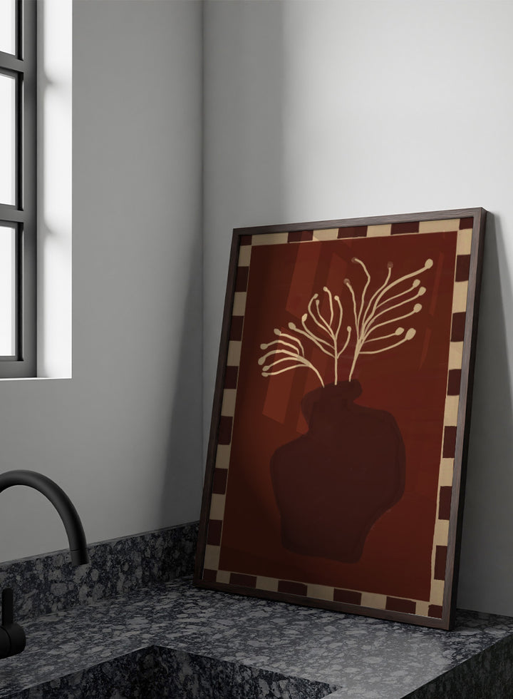 An art print featuring a dark brown abstract vase with cream branching stems on a deep reddish-brown background, framed by a beige and dark brown checkered border. Minimalist Vase Plant by The Art Concept still life art print featuring a dark vase, cream stems, checkerboard border, and warm rust-brown tones.