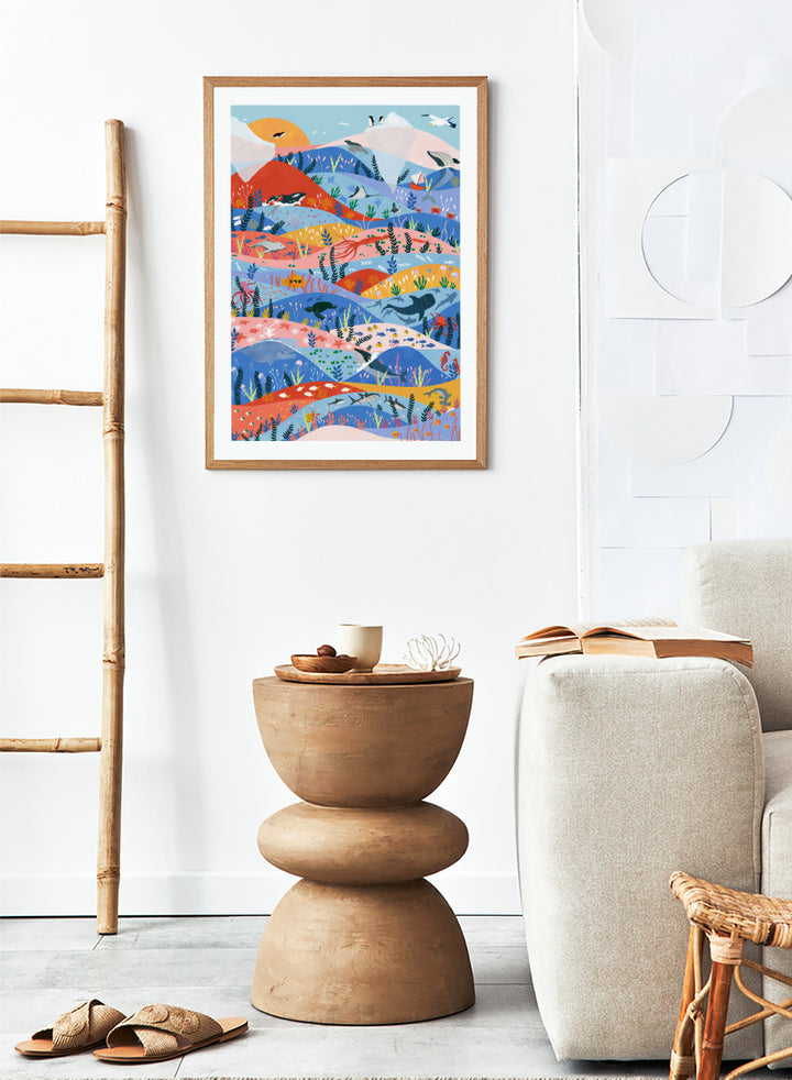 A colorful illustrated art print featuring stylized mountains, sea life, and coastal scenery in layered wavy bands of blue, pink, orange, yellow, and green. Vibrant Ocean Life by Ceyda Alasar ocean art print featuring whales, sharks, rays, turtles, coral reefs, sea plants, and colorful marine life.