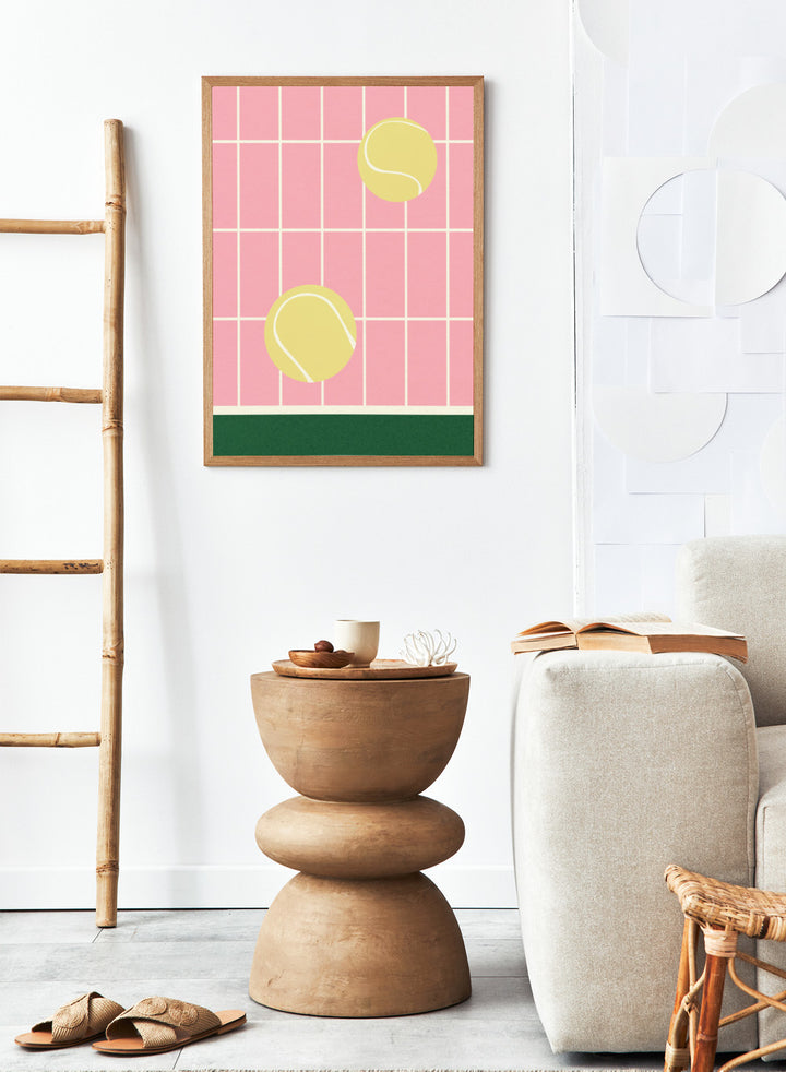 Two yellow tennis balls on a pink grid background with a green stripe at the bottom. Tennis Kitchen by Rosi Feist is a modern minimalist fine art print featuring oversized tennis balls on pink tile. Officially licensed wall poster with optional artisan framing.