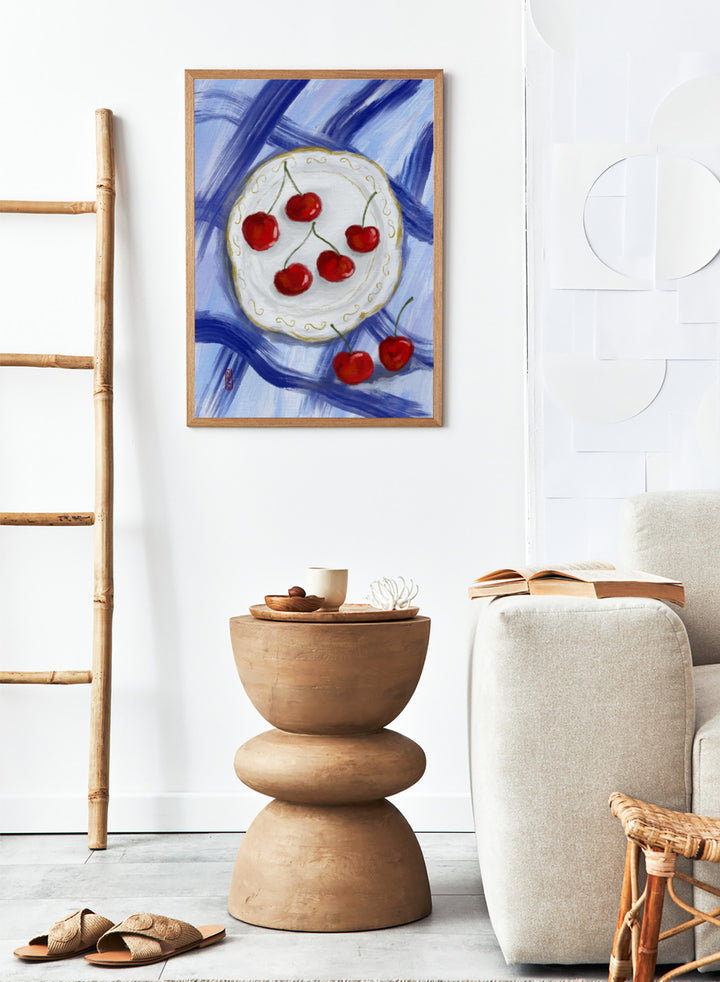 Painting of cherries on a white plate with a blue background. Red Cherries Blue Table by Dirkie Nell is a contemporary fruit still life art print featuring hand painted cherries, blue table linens, and colorful kitchen wall art style.
